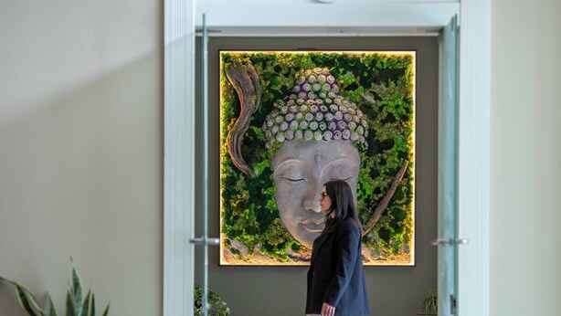Eine Person geht durch einen Flur mit einer großen Buddha-Statue und Pflanzen an der Wand.