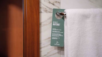 Un bagno con parete in marmo, porta in legno e un asciugamano appeso a un gancio con un'etichetta che recita 'RISPETTA LA NATURA!'.