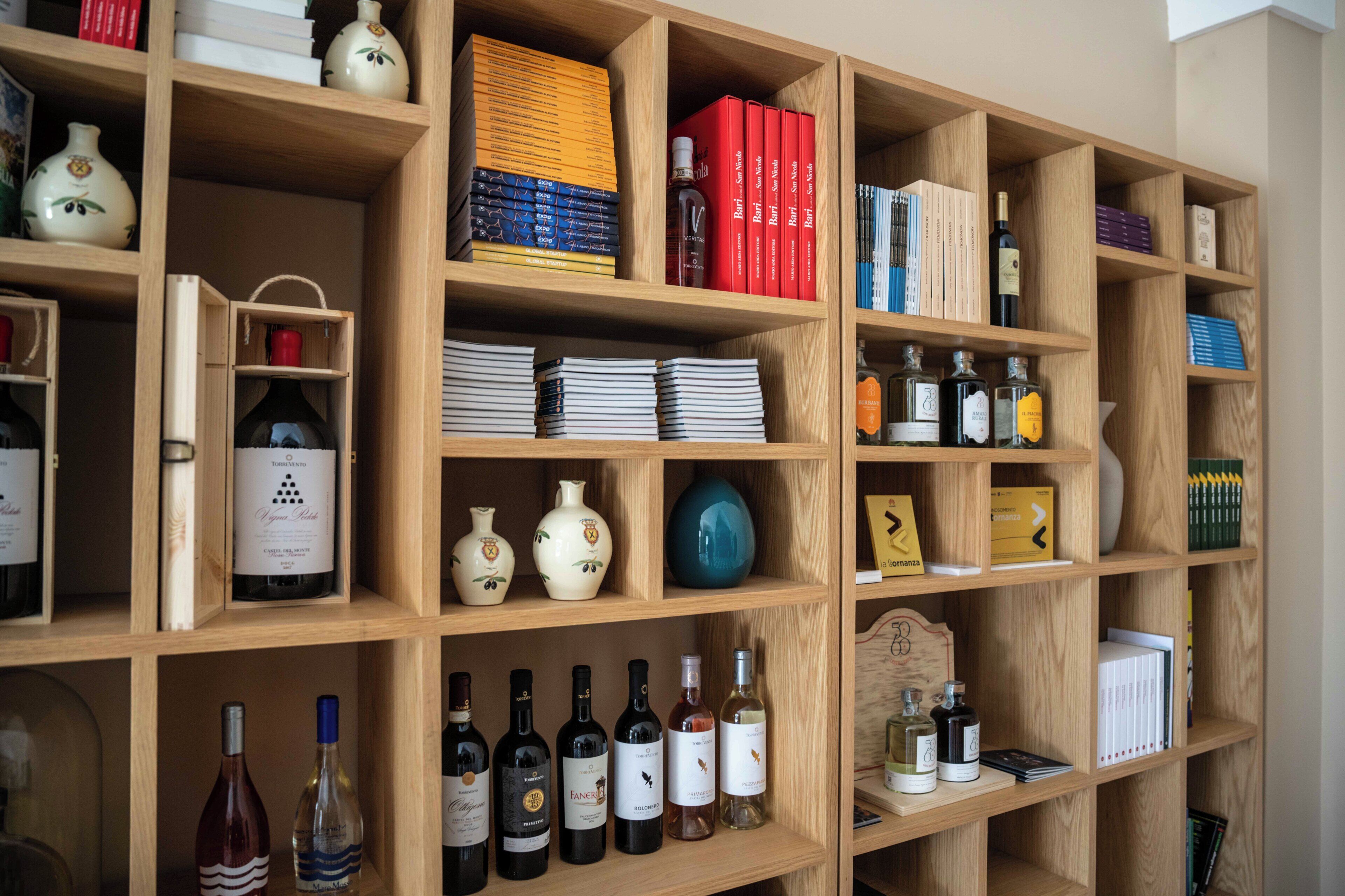 Una estantería de madera con libros, botellas de vino y jarrones decorativos.