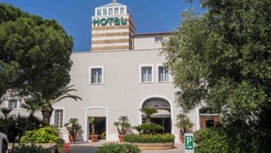 Ein Hotel mit einem auffälligen 'HOTEL'-Schild auf einem Turm, einem zentralen Eingang mit einem Rundbogen und einem Parkschild, das eine Richtung anzeigt.