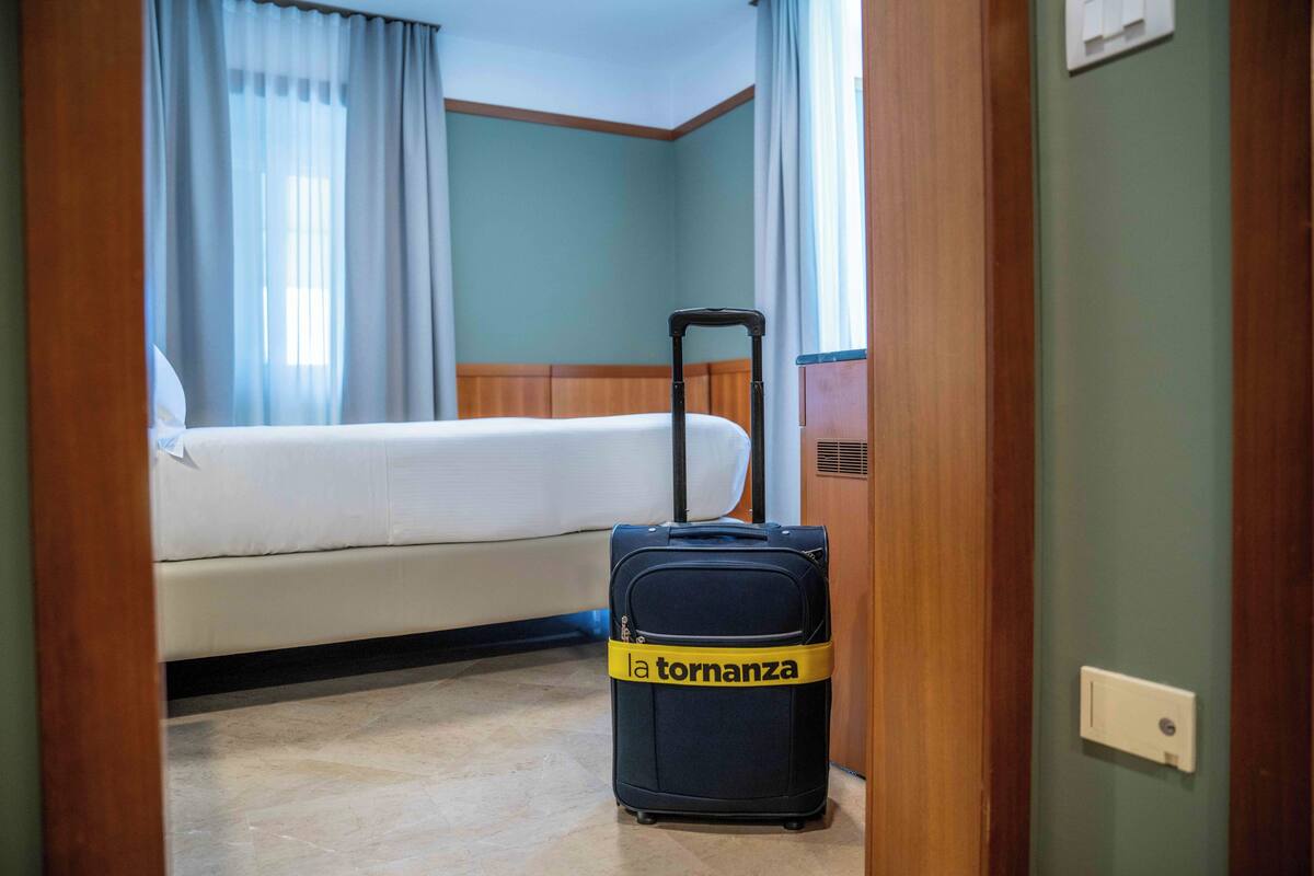 Una habitación de hotel con una cama, una maleta y una puerta.
