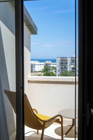 Un balcon avec une chaise et une table, d’où l’on peut admirer un immeuble et un ciel dégagé.