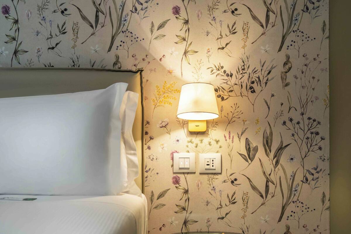Un dormitorio con cama, una lámpara de pared y una mesita con lámpara.