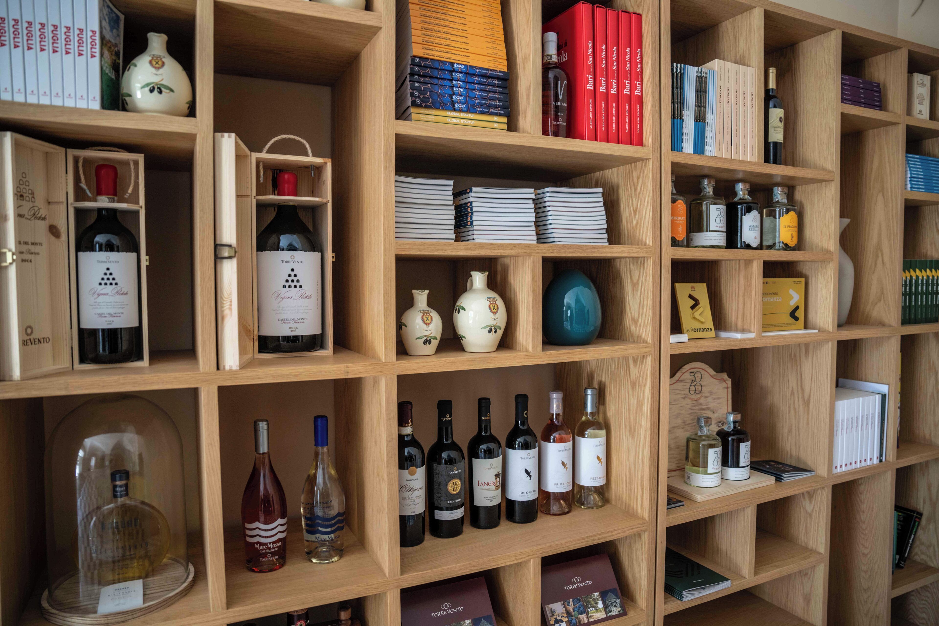 Una libreria in legno con diversi libri, bottiglie di vino e oggetti decorativi.