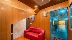 A room with wooden paneling, a red leather sofa, a framed picture, and a glass door leading to a hallway. - Vasantham Residency (Puducherry)