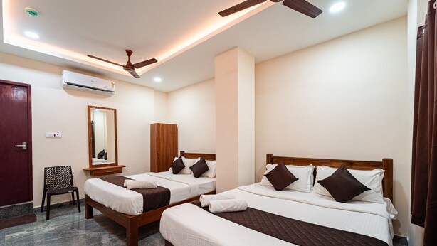 A hotel room with three beds, a ceiling fan, an air conditioner, a wooden wardrobe, a chair, and a mirror. - Vasantham Residency (Puducherry)