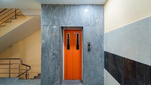A modern elevator with a distinctive orange door, surrounded by marble walls and a staircase. - Vasantham Residency (Puducherry)