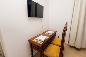 Une pièce avec une table à manger en bois, dressée pour deux personnes, un téléviseur fixé au mur et une chaise en bois avec un coussin jaune.