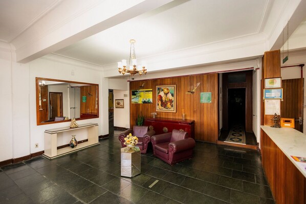 A lobby with a reception desk, a mirror, a chandelier, leather sofas, and a console table.