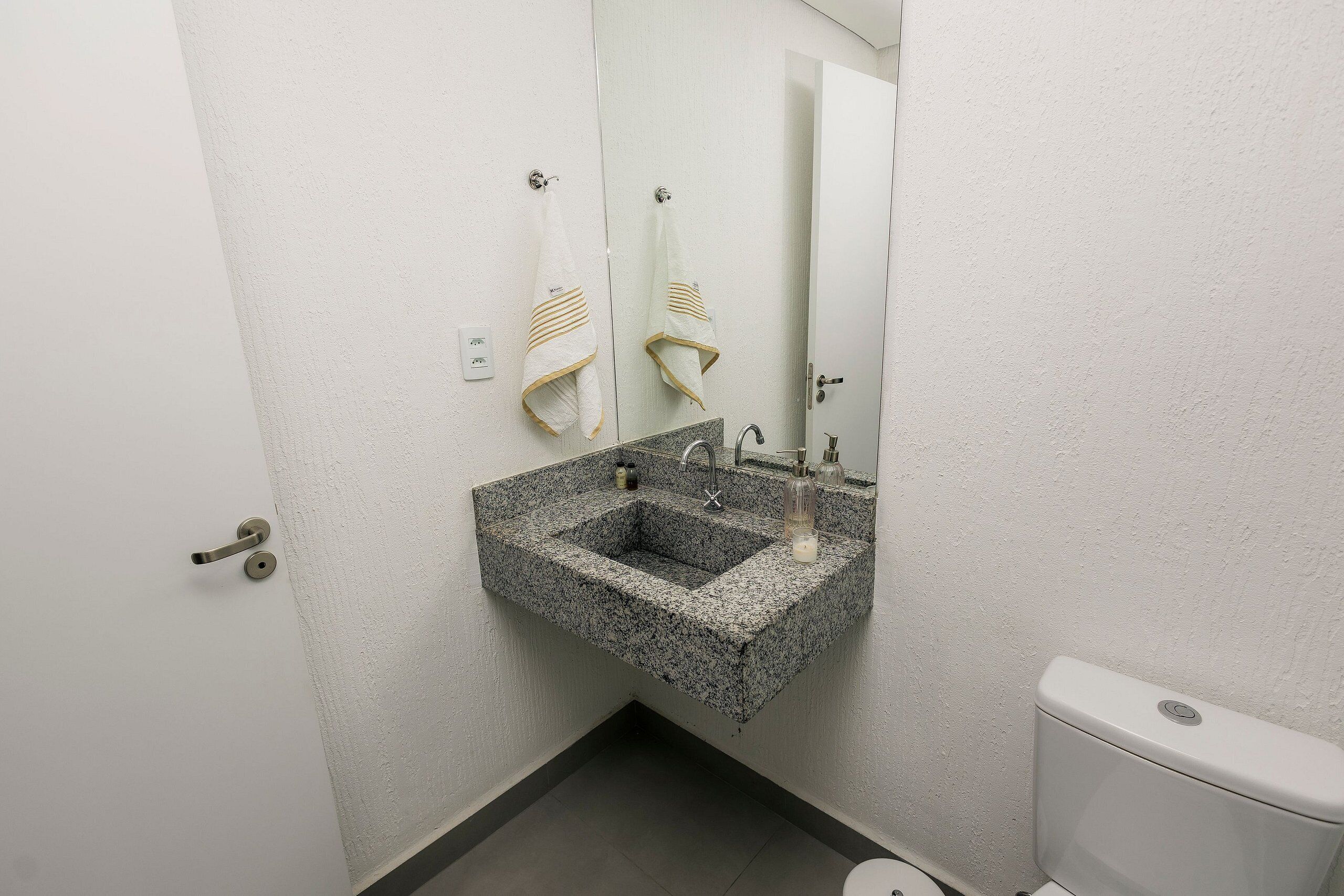 A bathroom with a granite sink, a mirror, a towel rack, and a toilet.