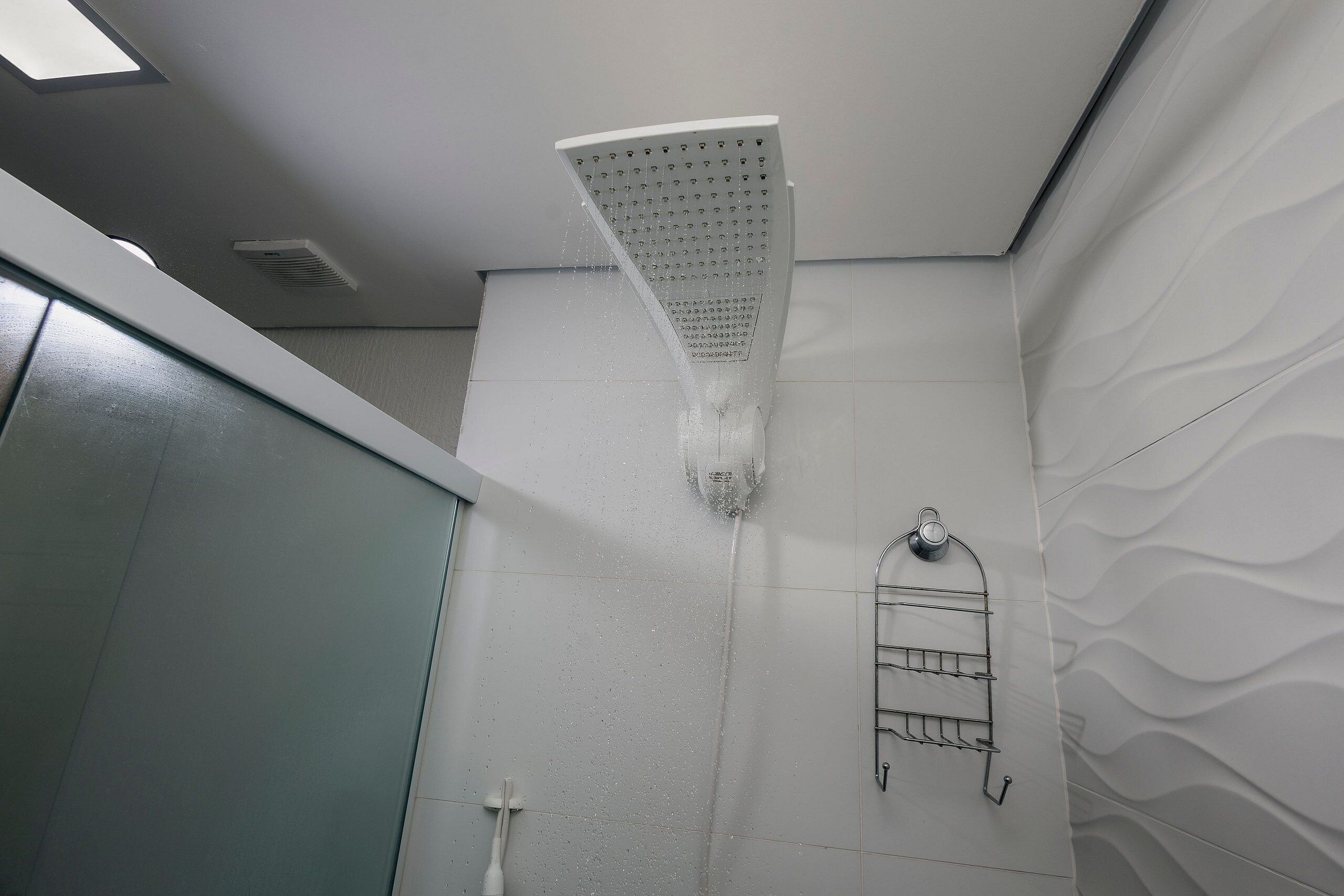A showerhead with water flow, a towel rack, and a textured wall.