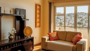 A living room with a sofa, a wooden cabinet, and a large window with a city view. - Prime Center View - Beautiful view. Do it all on foot! (São Lourenço)
