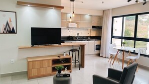 A modern living room with a flat-screen TV, wooden entertainment unit, and a dining area with a table and chairs.