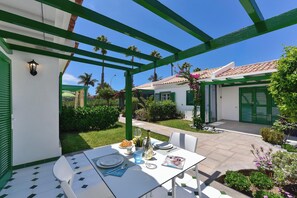 Eine Terrasse im Freien mit Esstisch, umgeben von viel Grün und blauem Himmel.