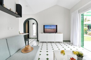 Ein modernes Wohnzimmer mit Fernseher, einer Couch und einem Esstisch mit einem Getränk und Obst.