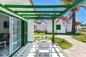 Eine Terrasse mit Esstisch, einem weißen Stuhl und einer grünen Pergola.