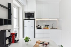 Eine moderne Küche mit weißen Schränken, einem Edelstahlkühlschrank, einer Kaffeemaschine und einem kleinen Topfpflanzen.