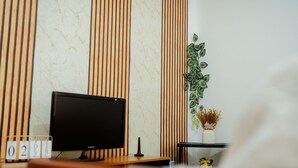 Una habitación moderna con televisor de pantalla plana, un escritorio de madera, una planta y un florero con flores secas.