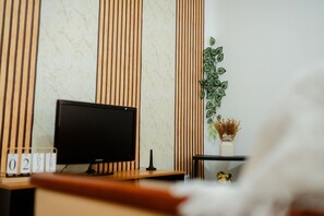 Una habitación moderna con televisor de pantalla plana, un escritorio de madera, una planta y un florero con flores secas.