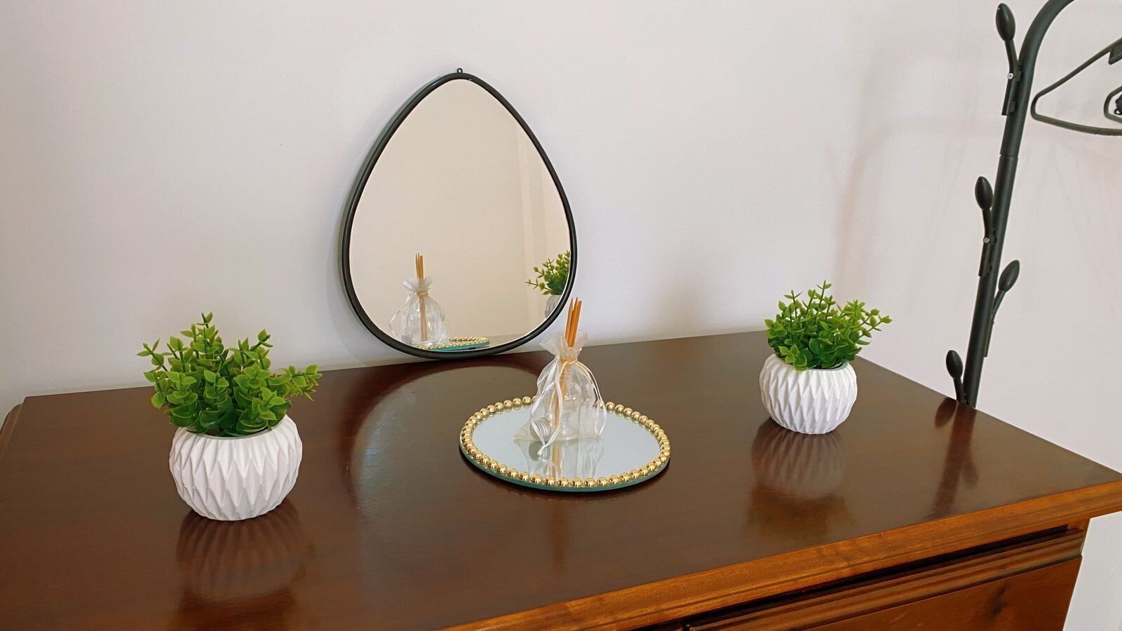 A wooden dresser with a mirror, two white vases with green plants, and a decorative item in the center.