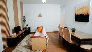 Una sala de estar moderna con sofá, televisor, mesita de madera y un comedor con sillas y mesa.