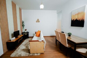 Una sala de estar moderna con sofá, televisor, mesita de madera y un comedor con sillas y mesa.
