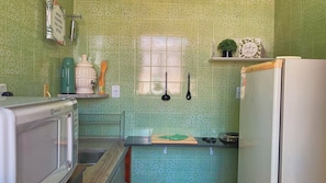 Una cocina con baldosas verdes estampadas, microondas, refrigerador, lavamanos y ventana.