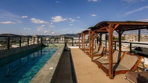 Una piscina en la azotea con agua azul cristalina, pérgolas de madera y sillones de descanso.