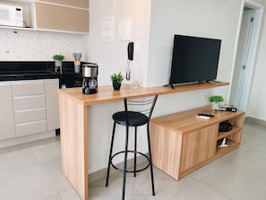 A compact kitchen with a microwave, coffee maker, and a TV on a wooden shelf.