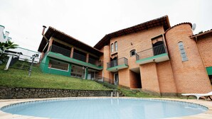 A swimming pool with a stone deck, a brick building with balconies, and a stone retaining wall. - Spacious Colonial House with Pool and Incredible View (São Lourenço)