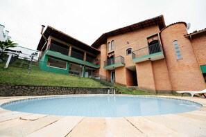 Ein Schwimmbecken mit einer Steindeck, ein Backsteinhaus mit Balkonen und eine Steinmauer.