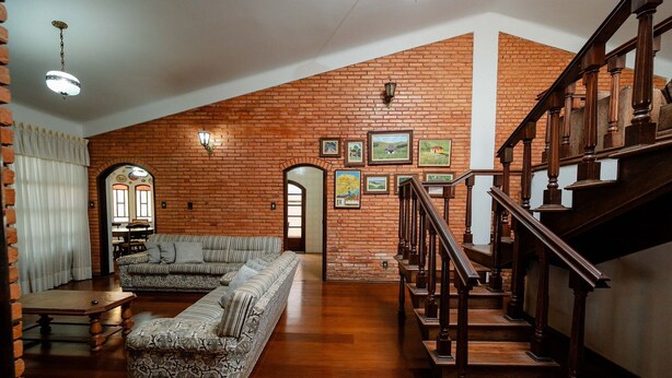 A spacious living area with a wooden staircase, a sectional sofa, and a brick wall with framed pictures. - Spacious Colonial House with Pool and Incredible View (São Lourenço)