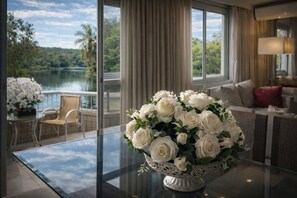 Una stanza con un tavolo in vetro, un bouquet floreale bianco, un divano e vista su un lago attraverso ampie finestre.