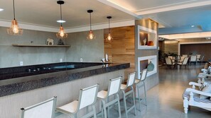 Une cuisine moderne dotée d’un bar, de tabourets de bar, de luminaires suspendus et d’un coin salon avec des chaises.