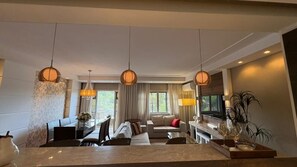 Un soggiorno moderno con zona pranzo, un divano, una TV e lampade a sospensione.
