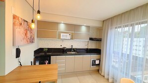A modern kitchen with a microwave, stove, and sink, a wooden dining table, and a large window with sheer curtains.