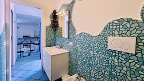 Ett badrum med en vägg täckt av mosaik, ett handfat och en spegel.