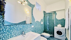 Ett badrum med en vägg täckt av mosaikplattor, ett vitt badkar, en toalett, en duschkabin och en tvättmaskin.