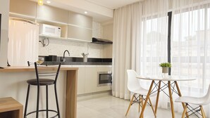A modern kitchen with a microwave, stove, and sink. There are two chairs and a small table with a plant. - Brand New Flat in the City Center with Air Condit. (São Lourenço)