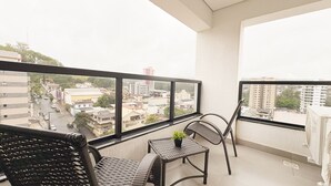 A balcony with a table and chairs, a potted plant, and a view of a cityscape. - Brand New Flat in the City Center with Air Condit. (São Lourenço)