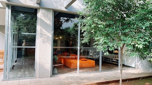 A modern building with large glass doors, an orange seating area, and a tree outside.