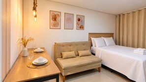 A hotel room with a bed, a sofa, a dining table with plates and glasses, and wall art.