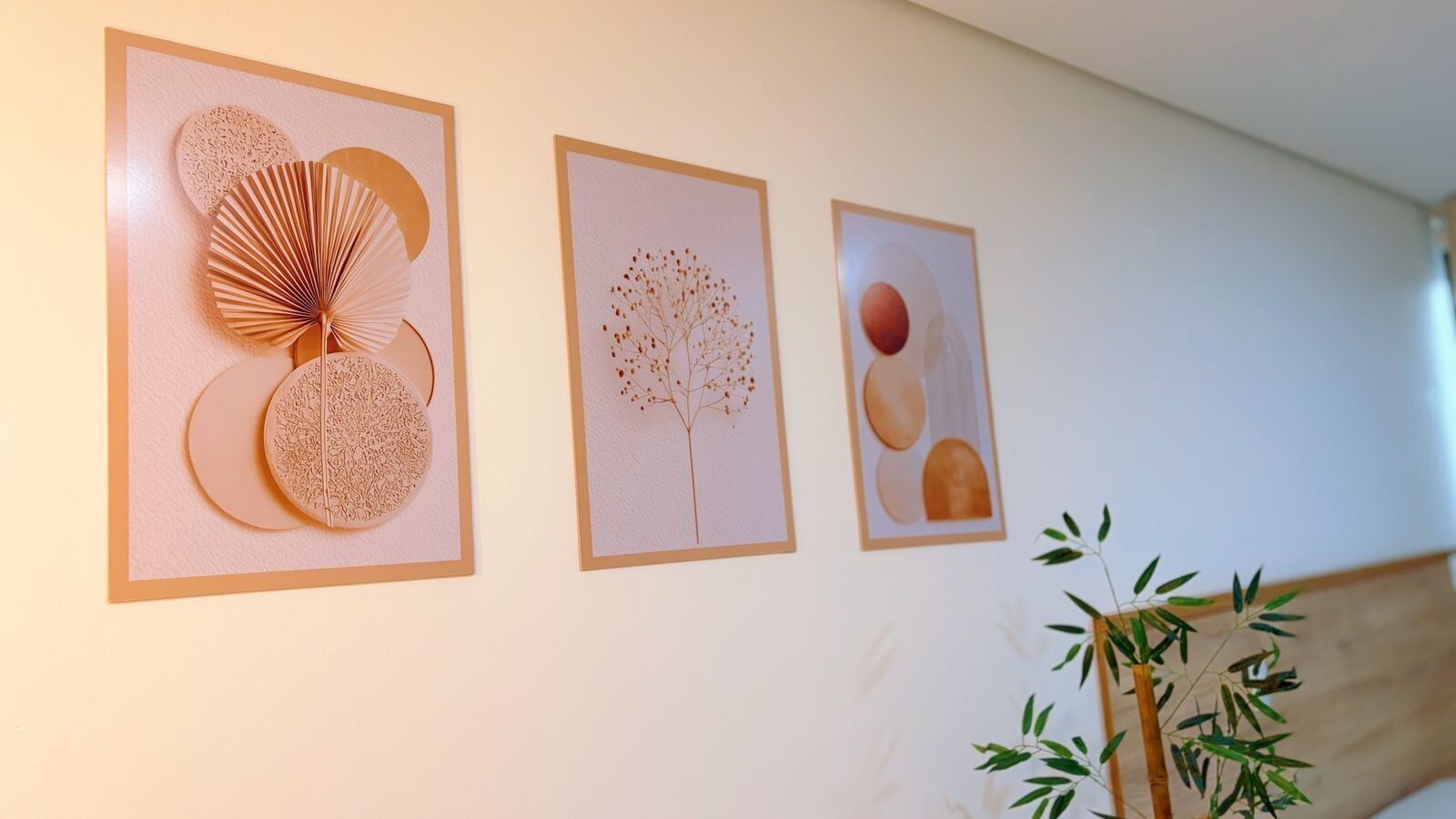 Tres obras de arte enmarcadas en una pared, una planta en maceta y un cabecero de madera.