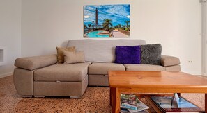 A living room with a sofa, a coffee table, and a painting of a lighthouse on the wall. - Casa Atlántida (Maspalomas)