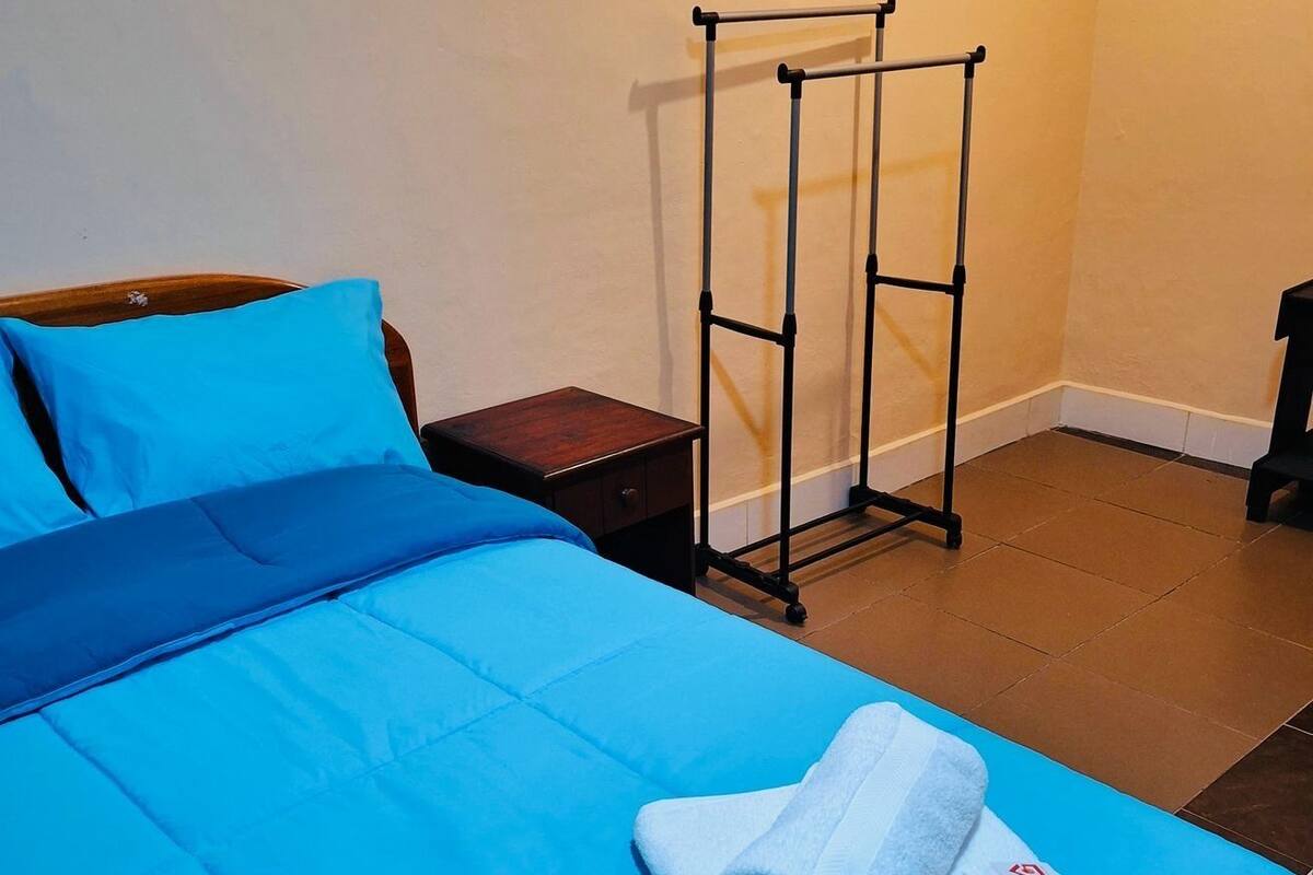 A bed with blue bedding, a wooden nightstand, and a black metal drying rack against a wall.