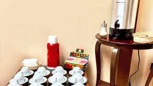 A wooden bench with white teapots, a red bottle, a box of tea, and a Hamilton Beach coffee maker on a wooden table. - Travel House Quito (Quito)