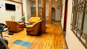 A spacious room with wooden flooring, a yellow sofa, a TV mounted on the wall, and a large window with a view. - Travel House Quito (Quito)