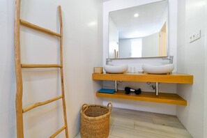 Ein Badezimmer mit einer Holzleiter, einem großen Spiegel, einem weißen Waschbecken und einem Korbwannenstuhl.