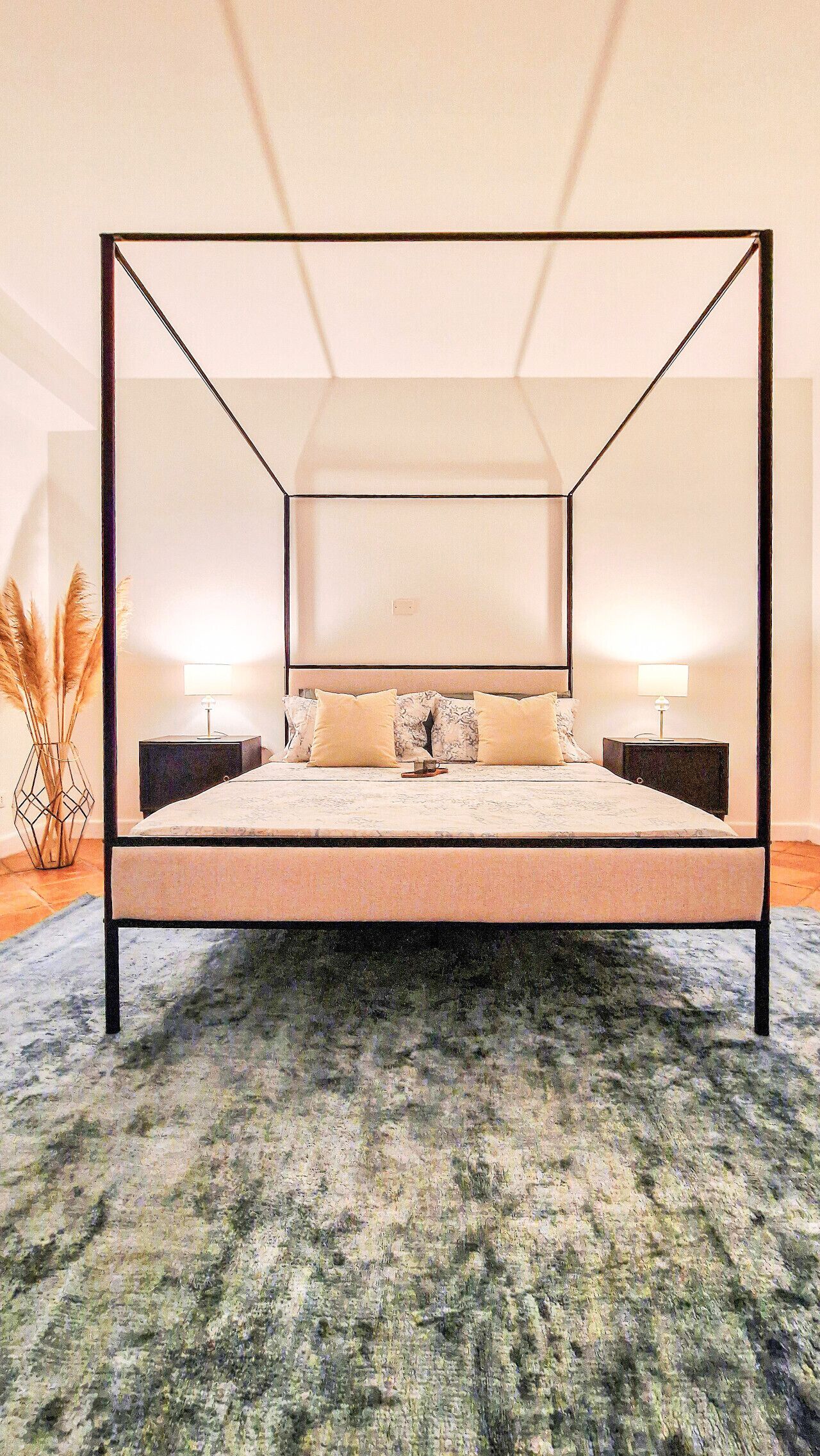 A four-poster bed with a marble headboard, two bedside tables, and a patterned rug.