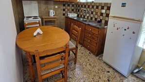Una cuina compacta amb armaris de fusta, taulell de granat i nevera blanca, i una taula de dinar amb caires.